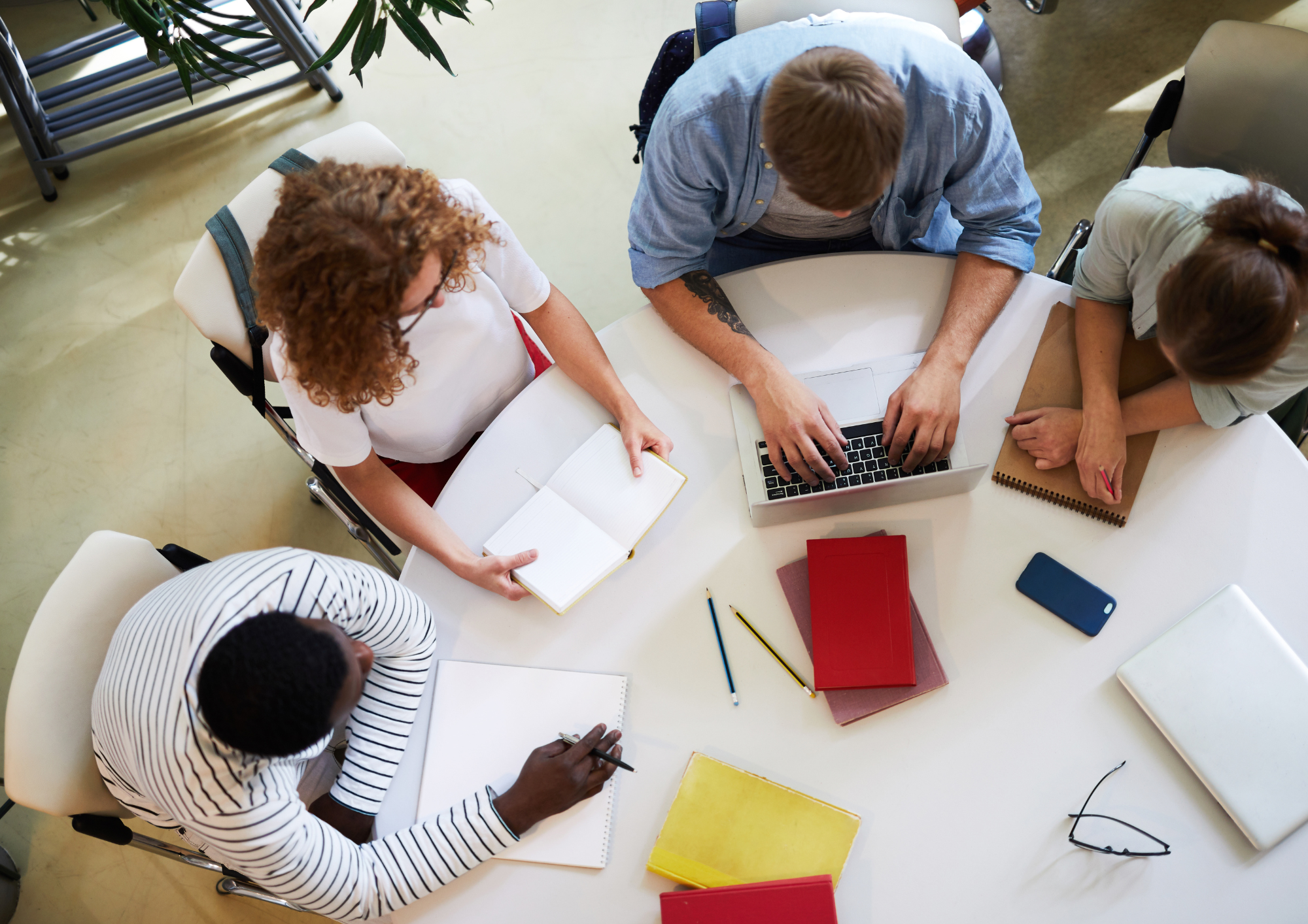 Four colleagues working together around a table with laptops and notebooks, seen from above