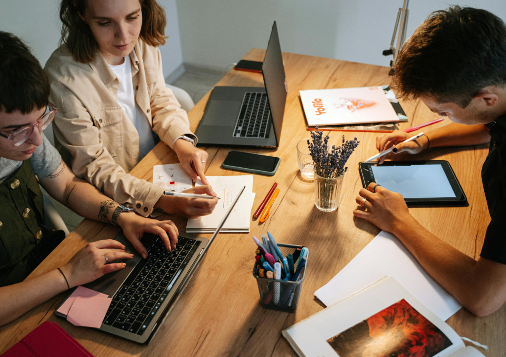 Four colleagues working together at a wooden table with laptops, a tablet and notebooks