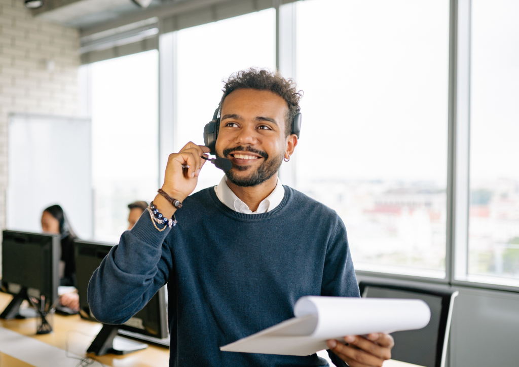 Smiling employee wearing a headset and holding documents in a bright open-plan office