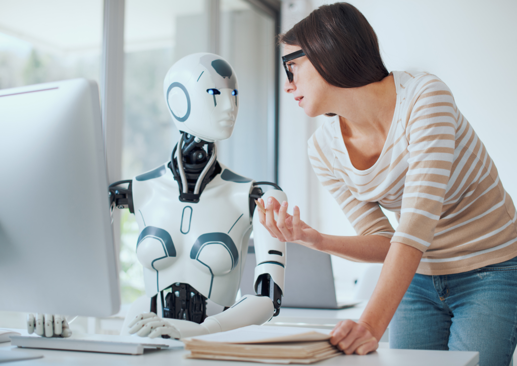 Woman at a desk working alongside a humanoid robot at a computer