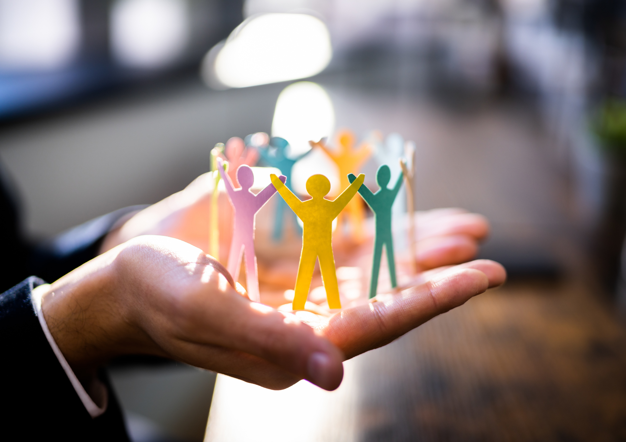 Hand holding colourful paper cut-out figures with their arms raised