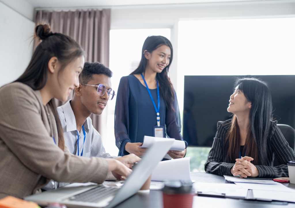 Colleagues smiling during a team meeting around a table with laptops and documents