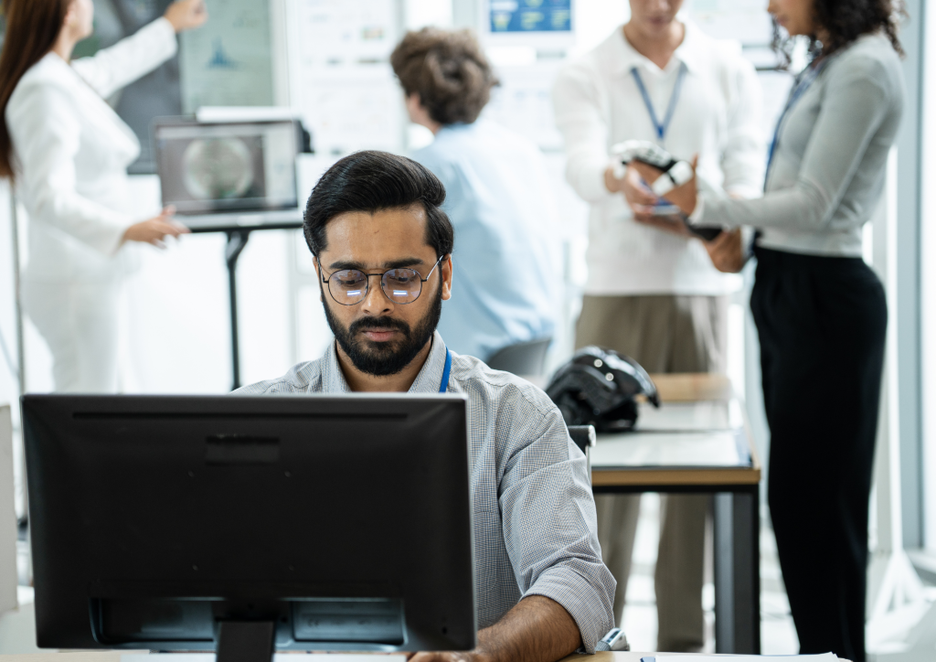 Employee working at a computer while colleagues test technology together in the background