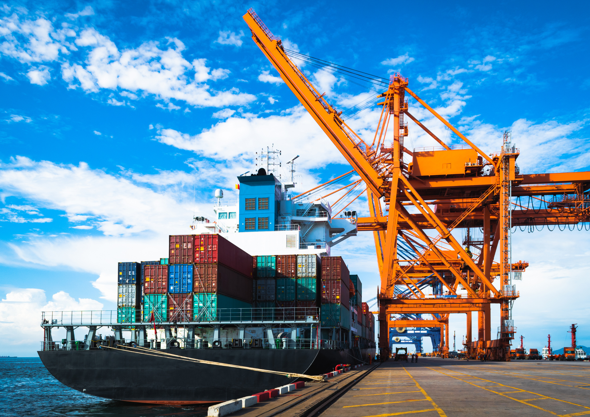 Container ship being loaded by orange gantry cranes at a port under a blue sky